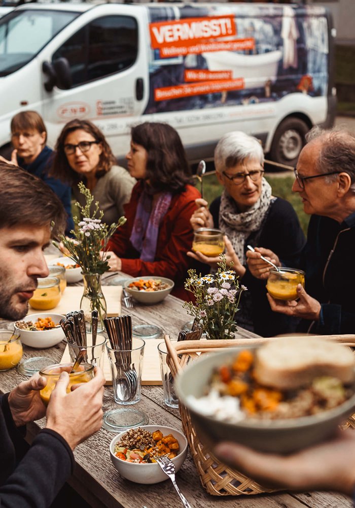 Ein langer Tisch an dem Menschen sitzen und essen.