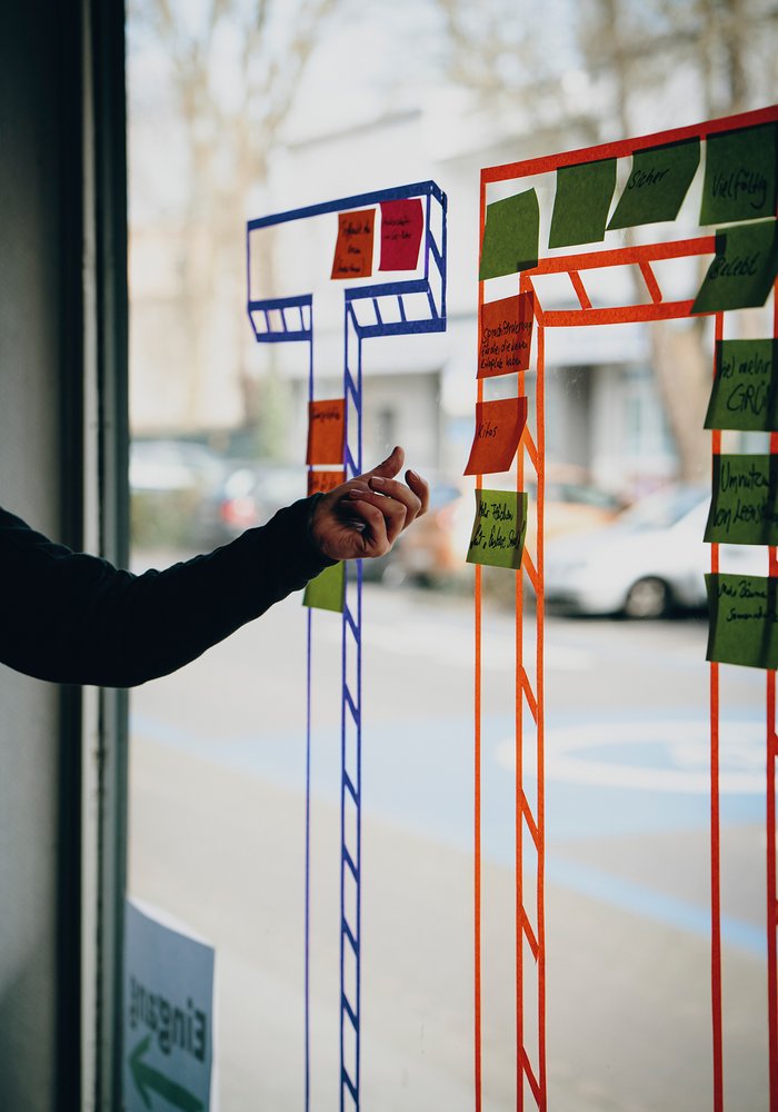 Ein Mensch, welcher Post Its an eine Scheibe klebt, an der mit bunten Klebeband TO steht.
