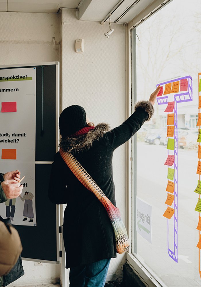 Drei Menschen kleben Post Its von innen an eine Fensterscheibe.