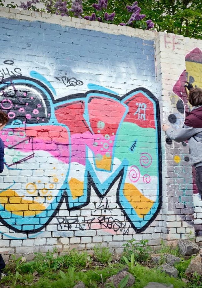 Zwei Menschen, die eine Wand mit Graffiti besprühen.