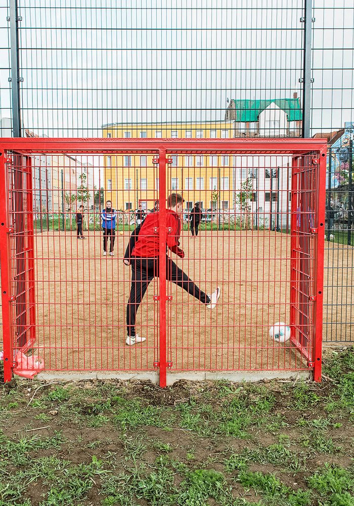 Ein Fußballfeld, auf dem Jugendliche zusammen Fußball spielen. Man sieht das Tor von hinten.