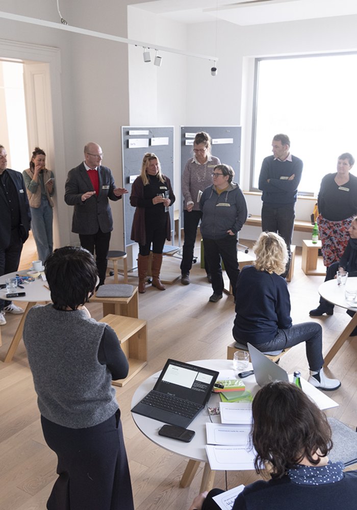 Ein Raum gefüllt mit stehenden Menschen, die eine Meeting haben.