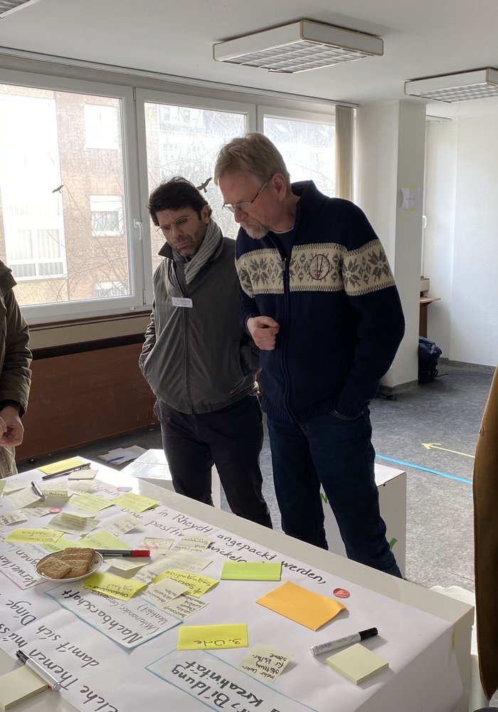 Fünf Menschen stehen um einen Tisch mit Notizen und diskutieren.
