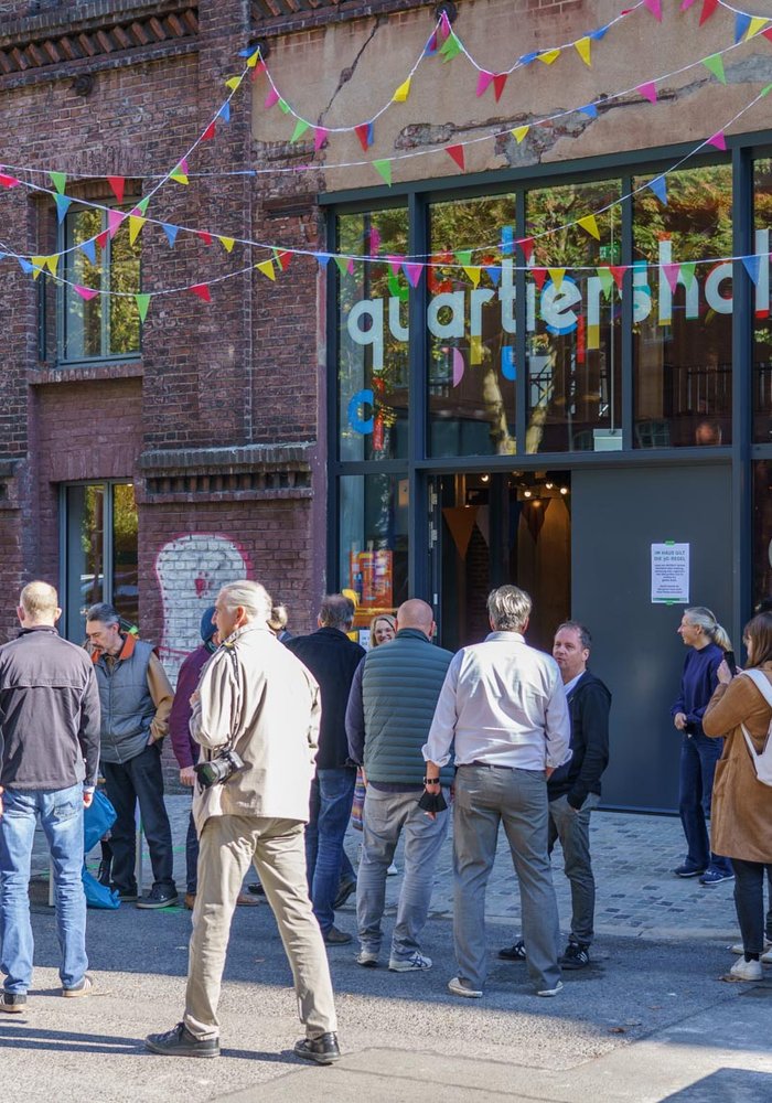 Eine Gruppe Menschen die vor der Quartiershalle versammelt sind, welche mit Girlanden geschmückt ist.