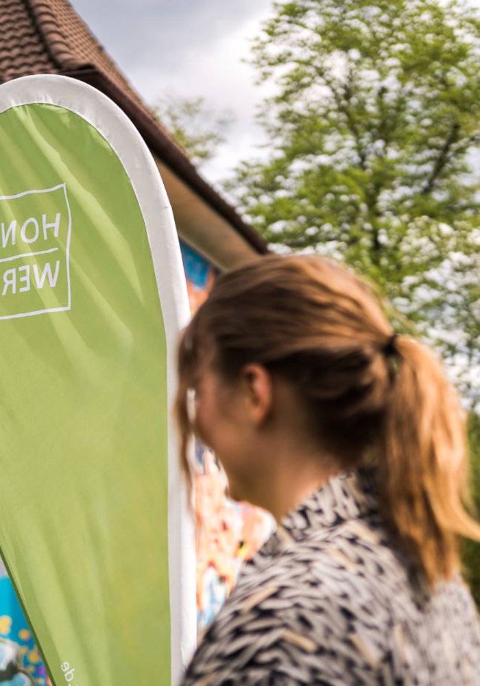 Eine Frau steht vor einer großen Fahne mit dem HONSWERK Logo