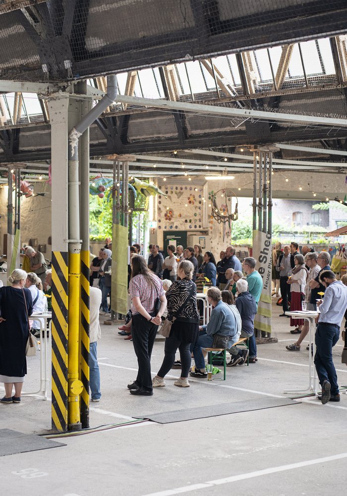 Die große geräumige Shedhalle, in der viele Menschen stehen und sich einen Vortag anhören.
